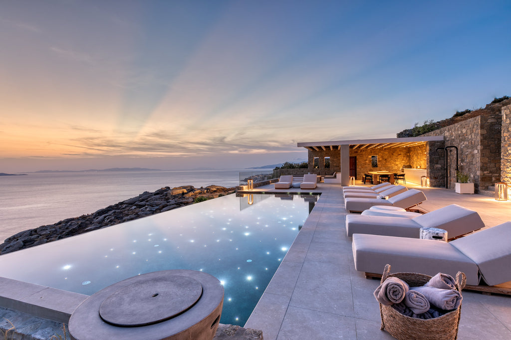 Luxury pool area with lounge chairs and ocean view at sunset.