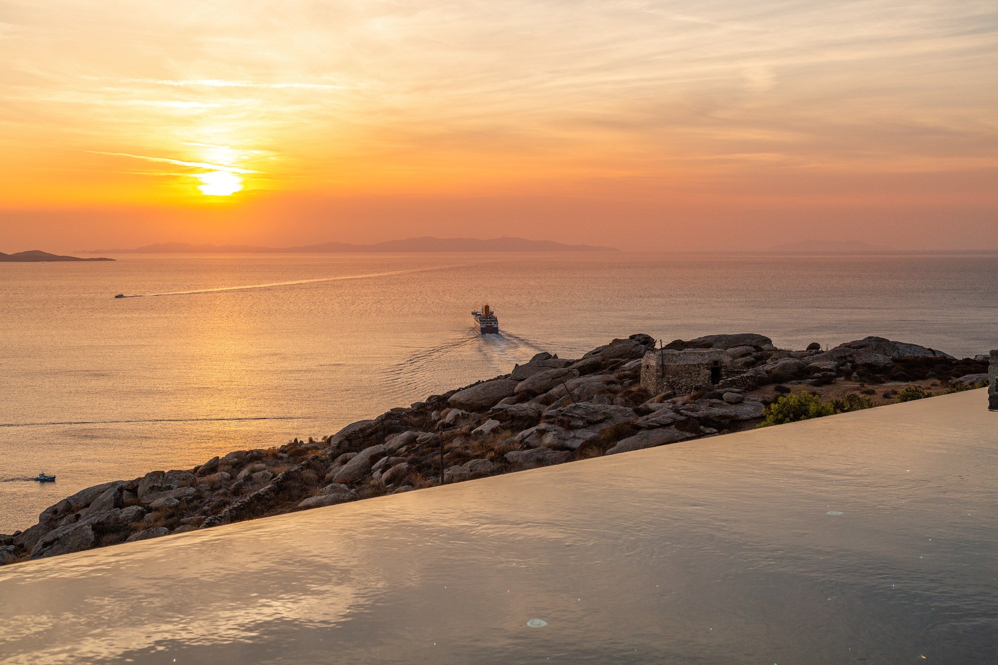 Sunset over a body of water with a boat and rocky shoreline.