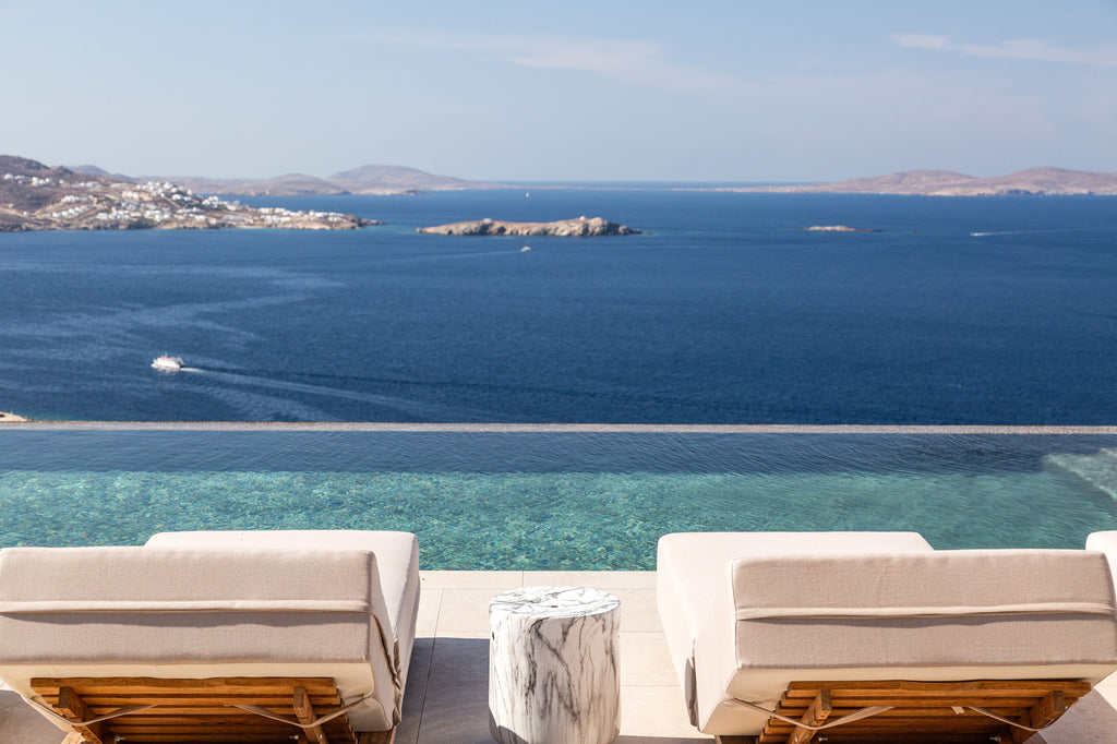 Two lounge chairs by a pool with a scenic view of the ocean and islands.