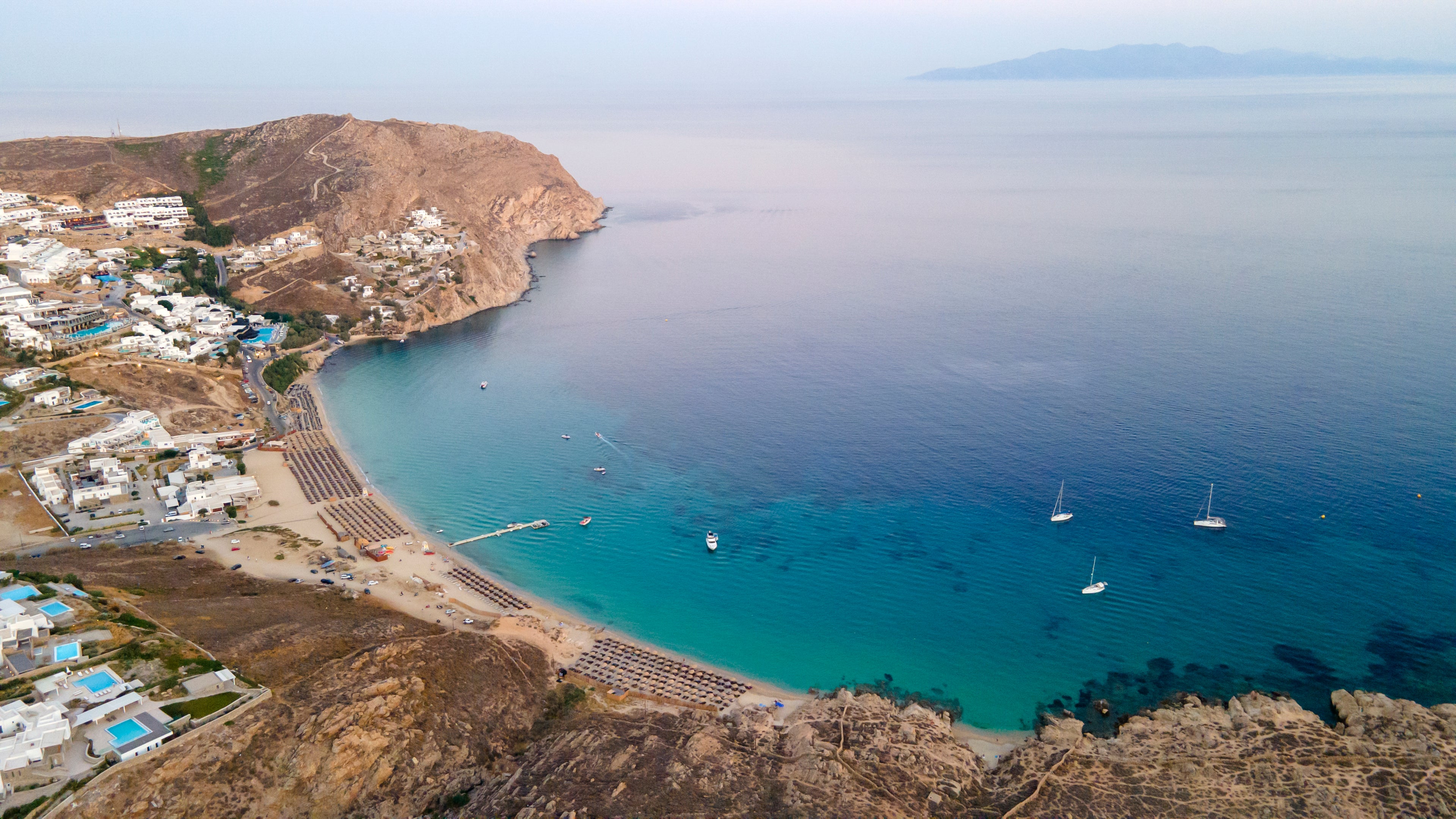 Coastal scene with a beach, clear blue water, and sailboats.
