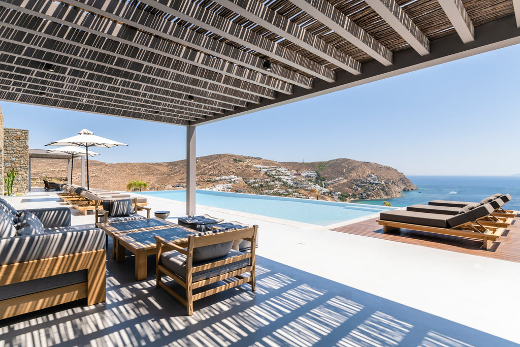 Outdoor patio area with pool, chairs, and table under a large pergola with ocean view.