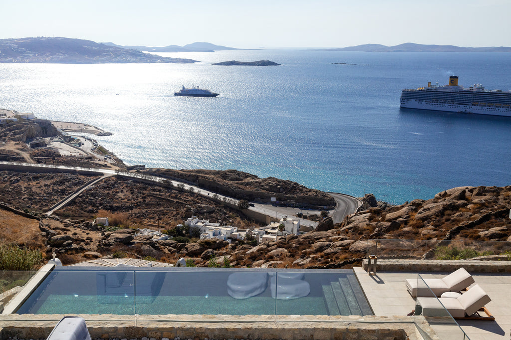 Modern pool with lounge chairs overlooking a scenic coastal view with boats and distant islands.