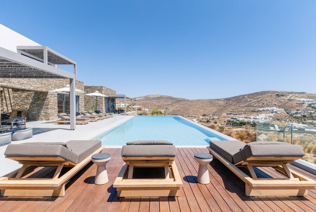 Outdoor seating area with wooden chairs and cushions by a pool with a scenic view.