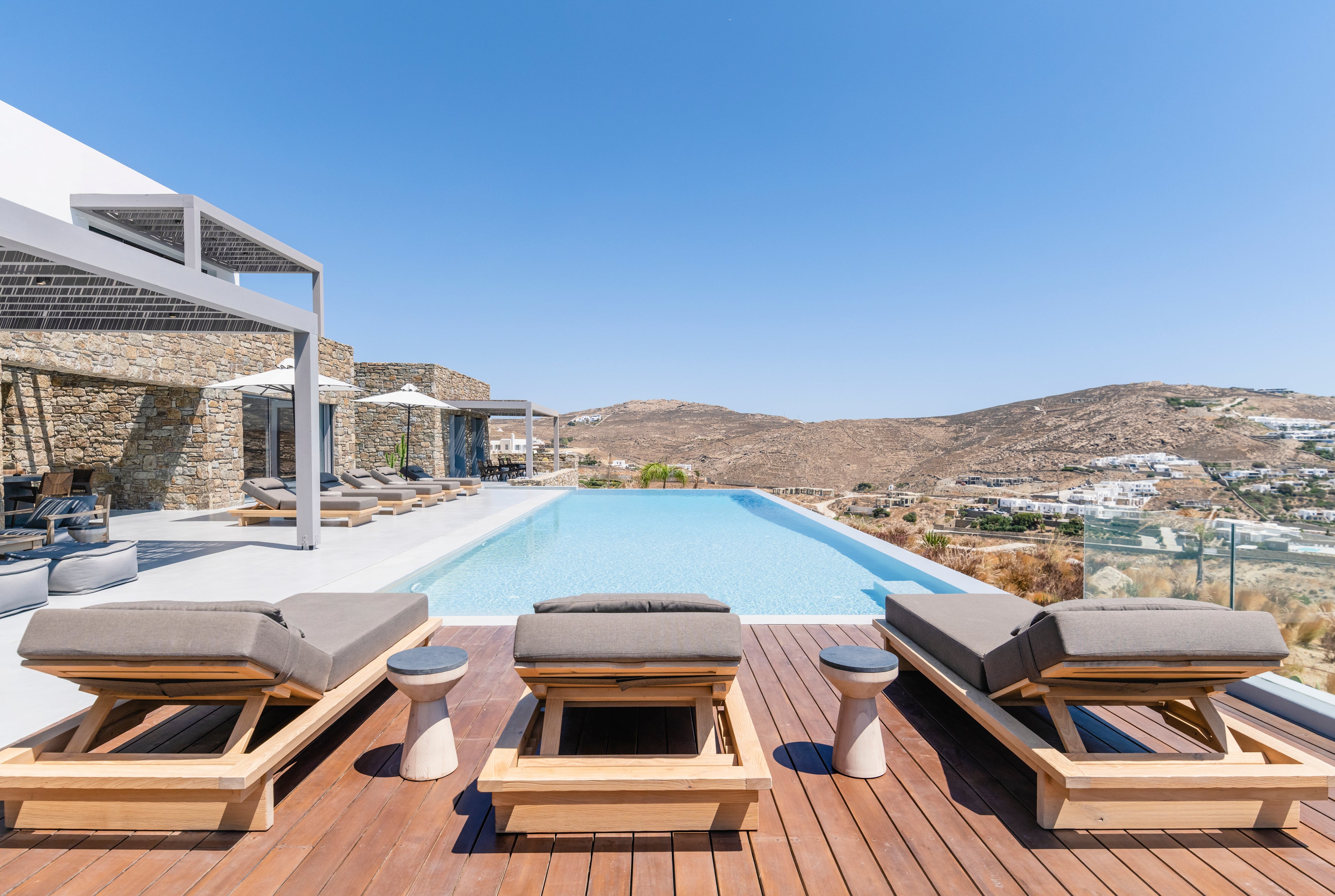 Outdoor seating area with wooden chairs and cushions by a pool with a scenic view.