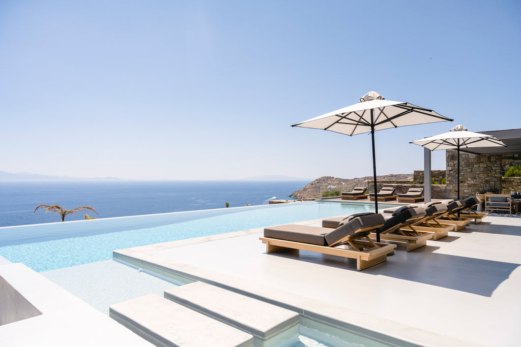 Outdoor pool area with lounge chairs and umbrellas overlooking the ocean.
