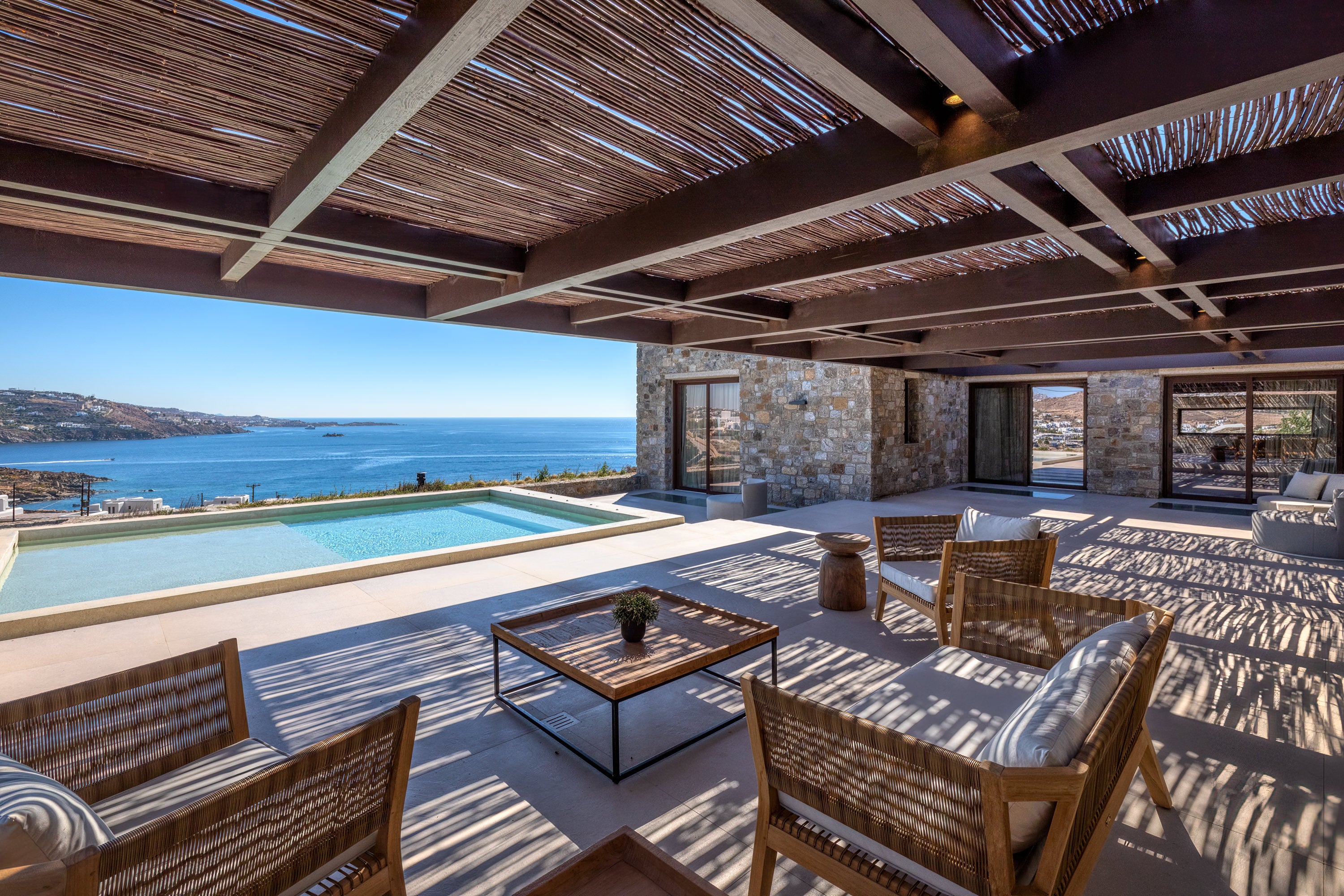 Outdoor patio area with ocean view, wooden furniture, and stone walls.