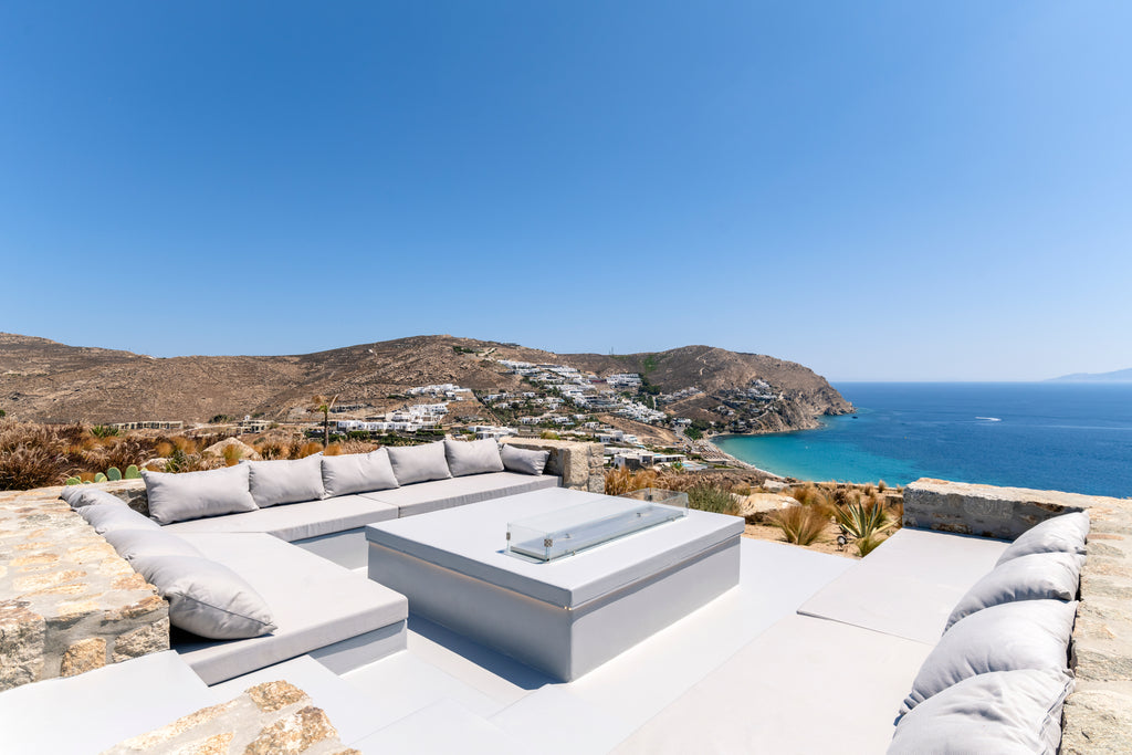 Outdoor seating area with a fire pit on a rooftop overlooking the ocean and hills.