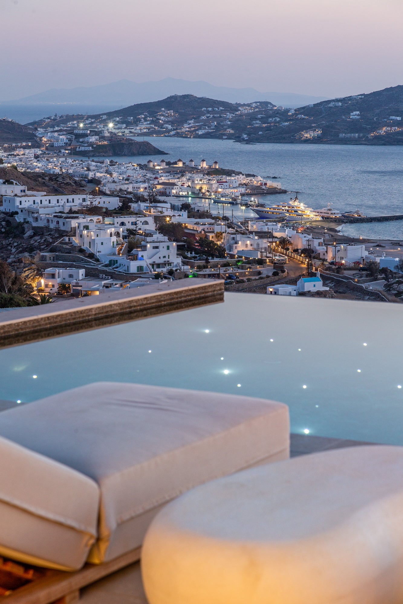 Infinity pool with a scenic view of a coastal town at dusk.