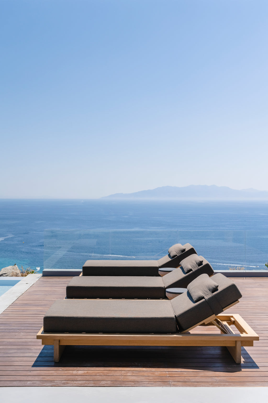 Outdoor lounge chair with cushions on a wooden deck overlooking the ocean.