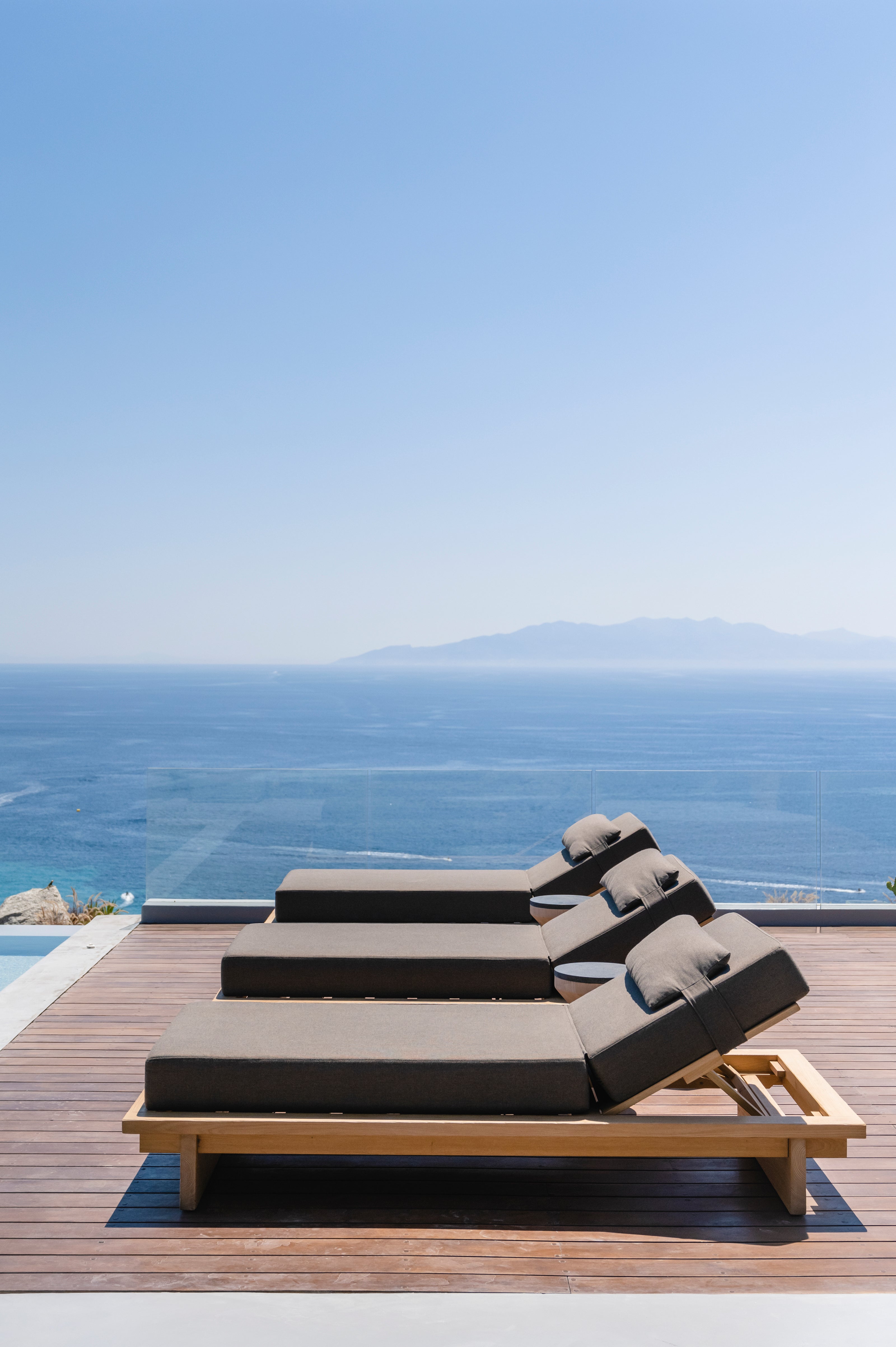 Outdoor lounge chair with cushions on a wooden deck overlooking the ocean.