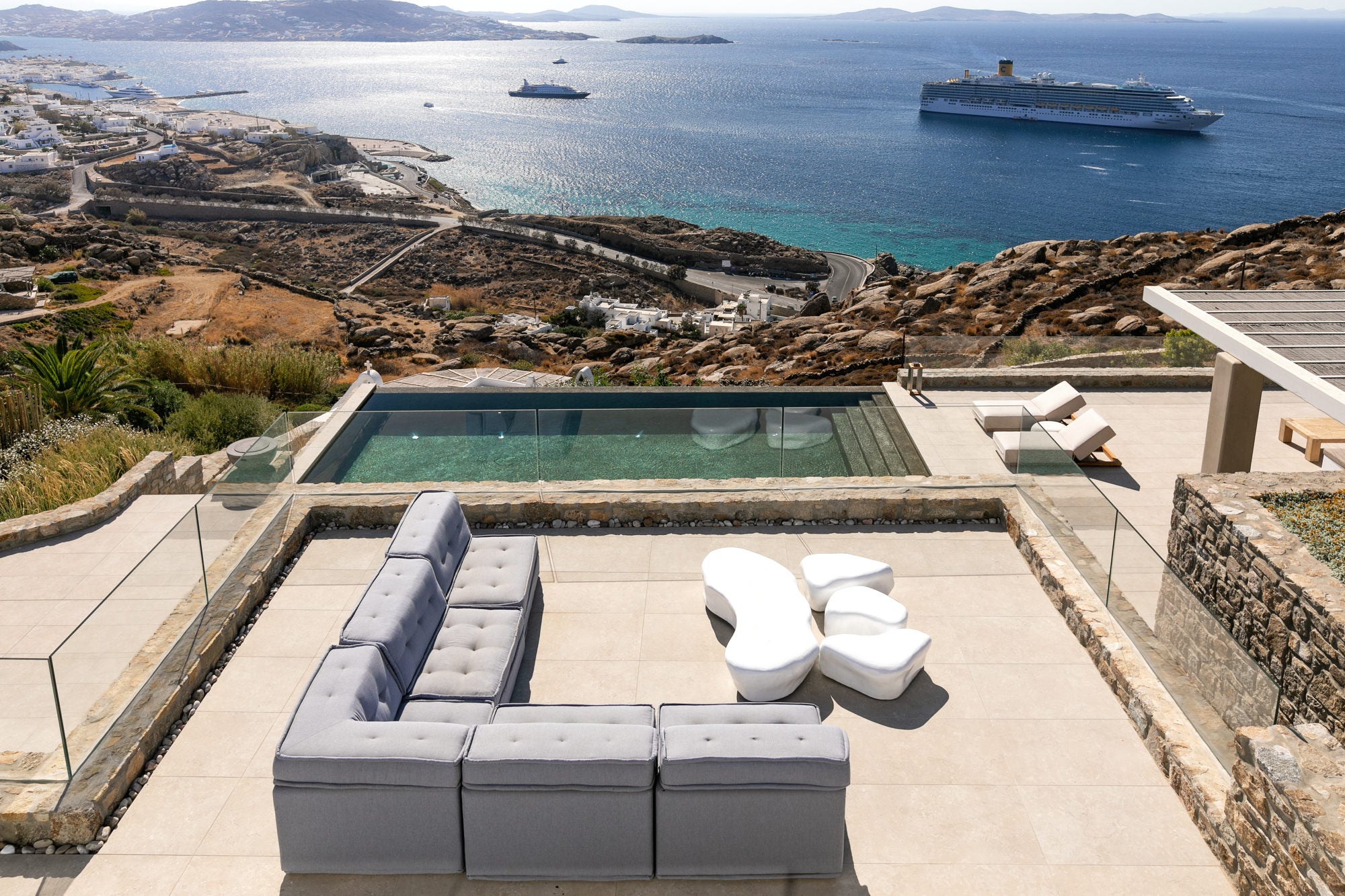 Outdoor seating area with a pool overlooking the sea and coastline.