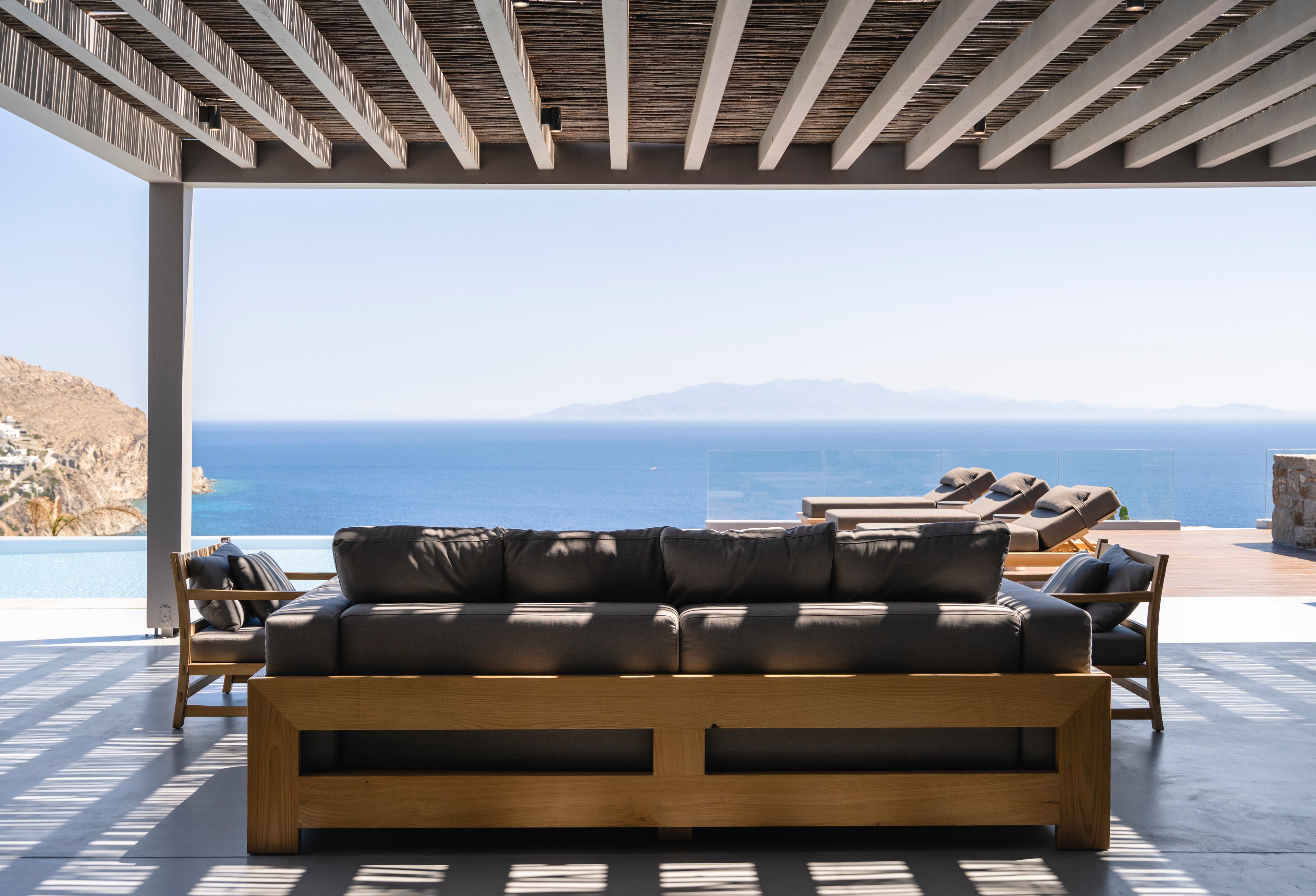 Outdoor wooden sofa with cushions on a patio overlooking the ocean.