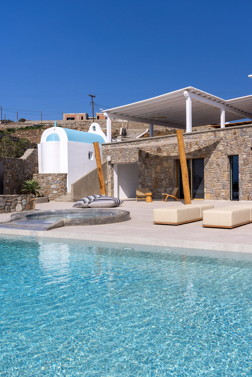 Pool area with lounge chairs, sun umbrellas, and a stone building under a clear blue sky.
