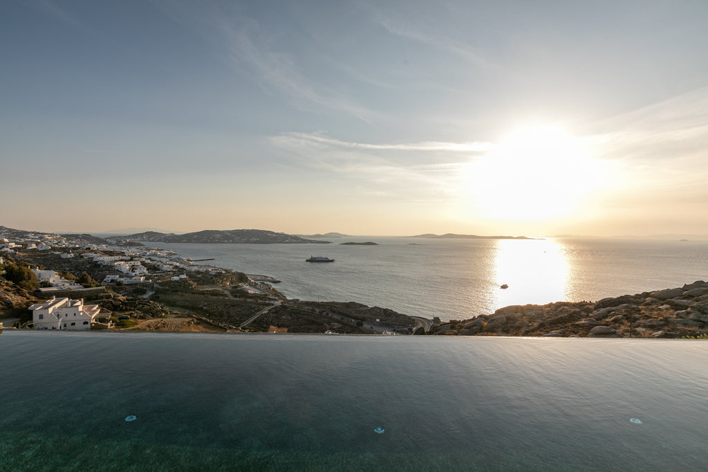Sunset over a coastal landscape with houses and a boat on the water.