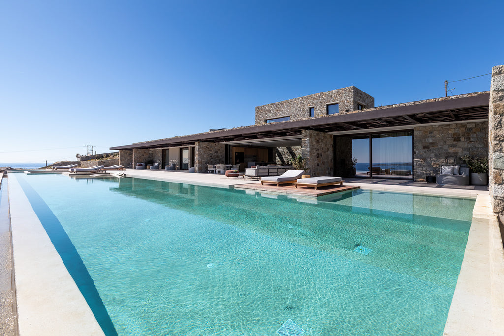 Modern house with a large pool area and outdoor furniture under a clear blue sky.