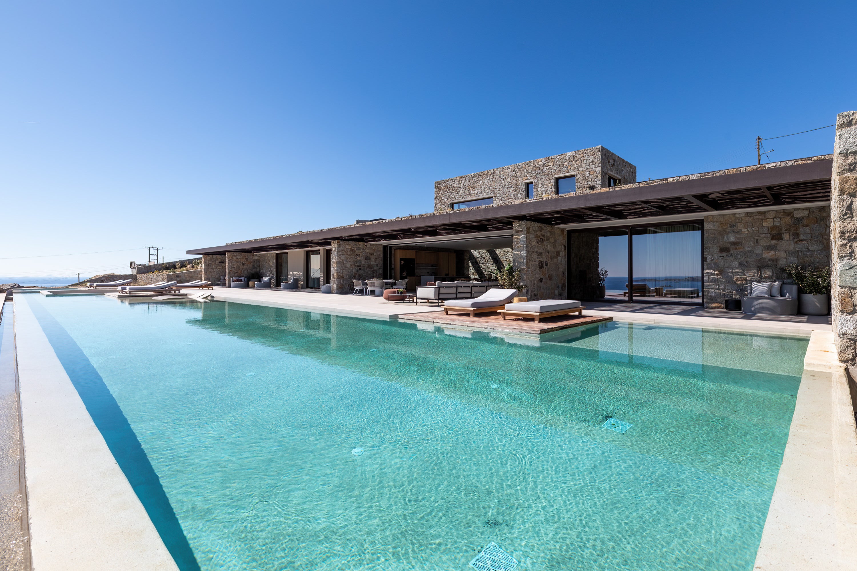 Modern house with a large pool area and outdoor furniture under a clear blue sky.