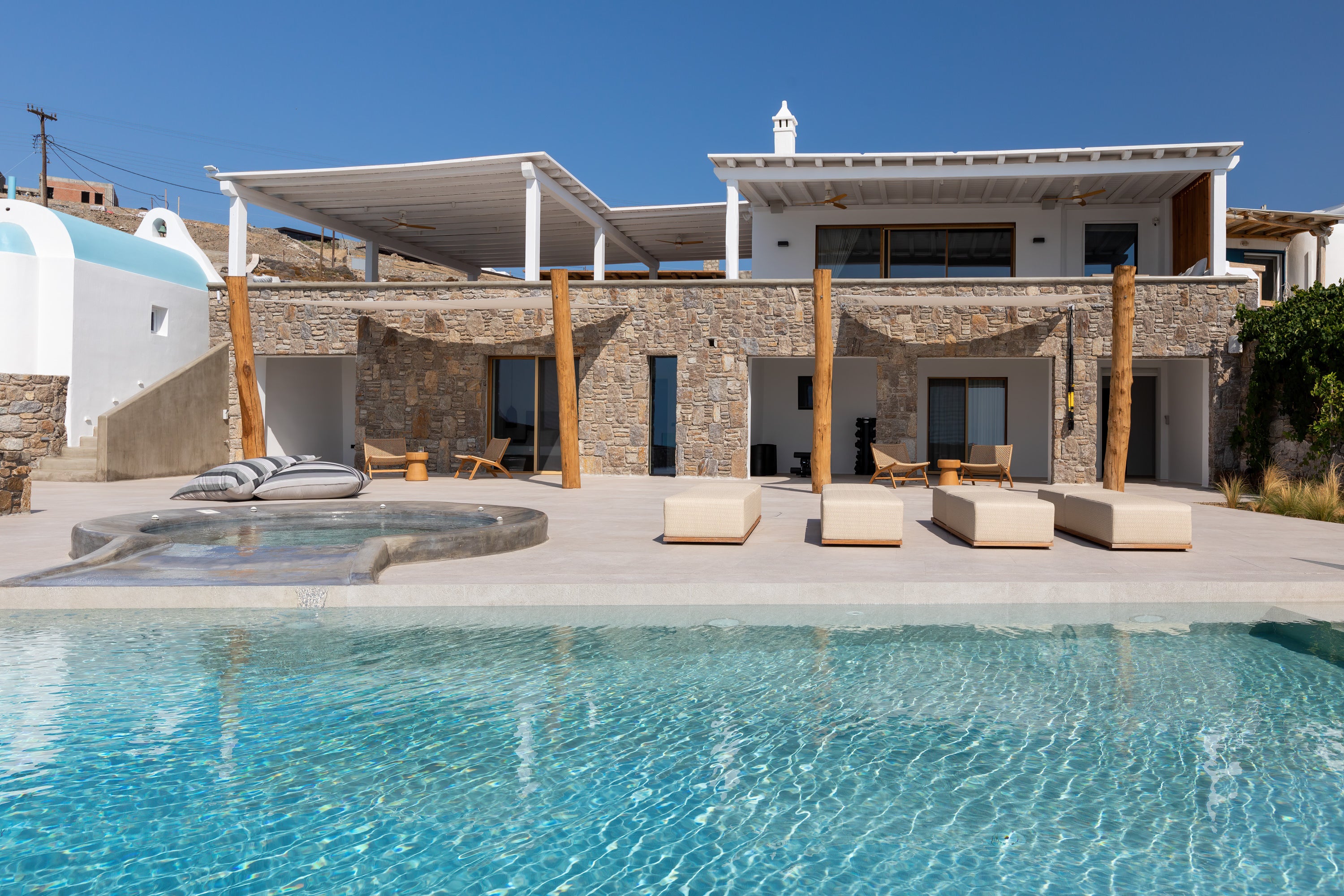 Luxury villa with pool and outdoor seating area under a clear blue sky.