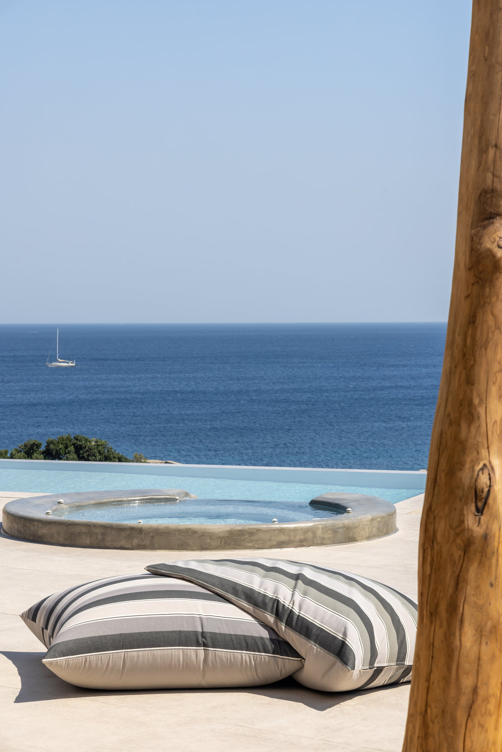 Striped pillows on a sun lounger with a pool and ocean view.