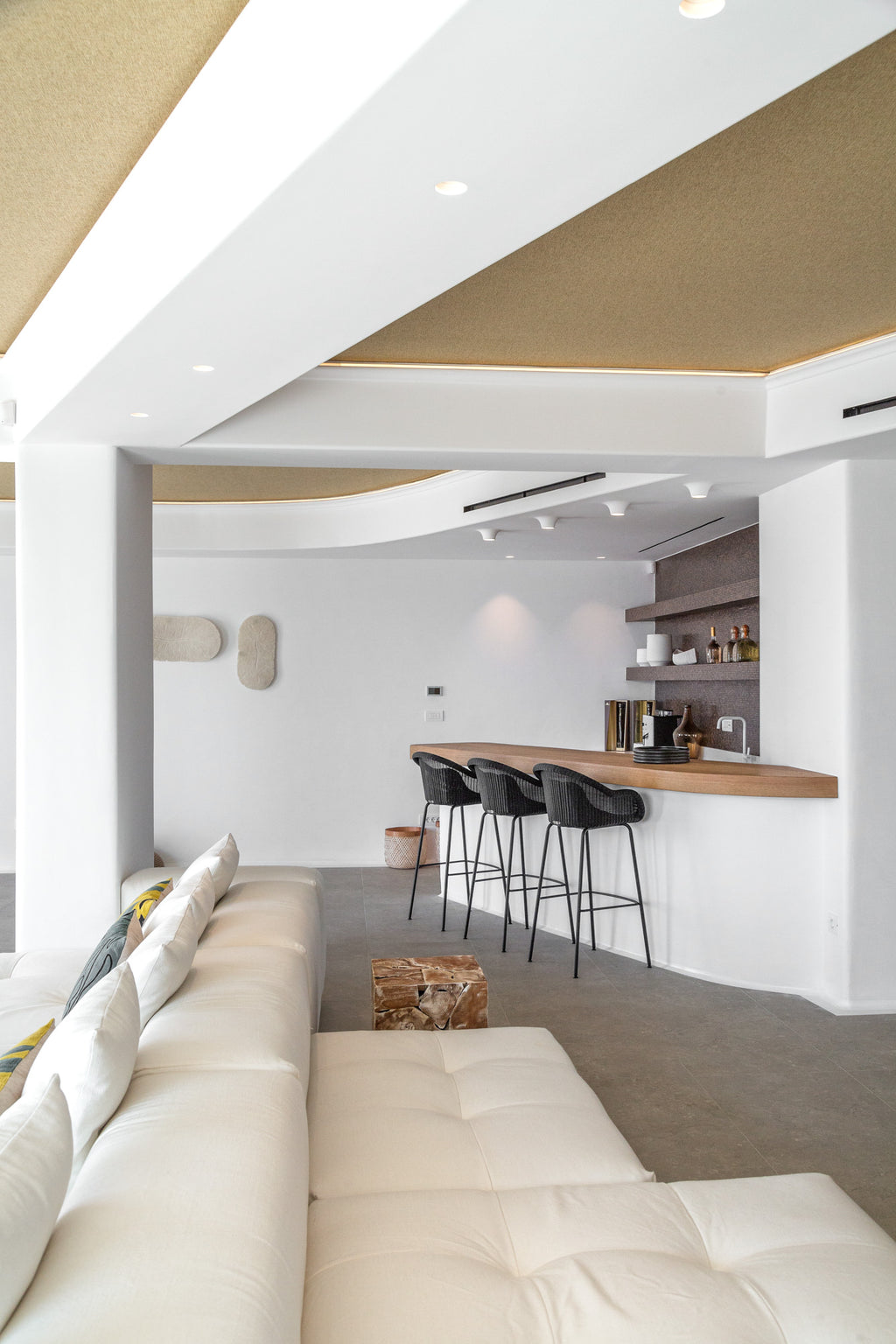 Modern living room with white sofa, kitchen bar, and black stools.