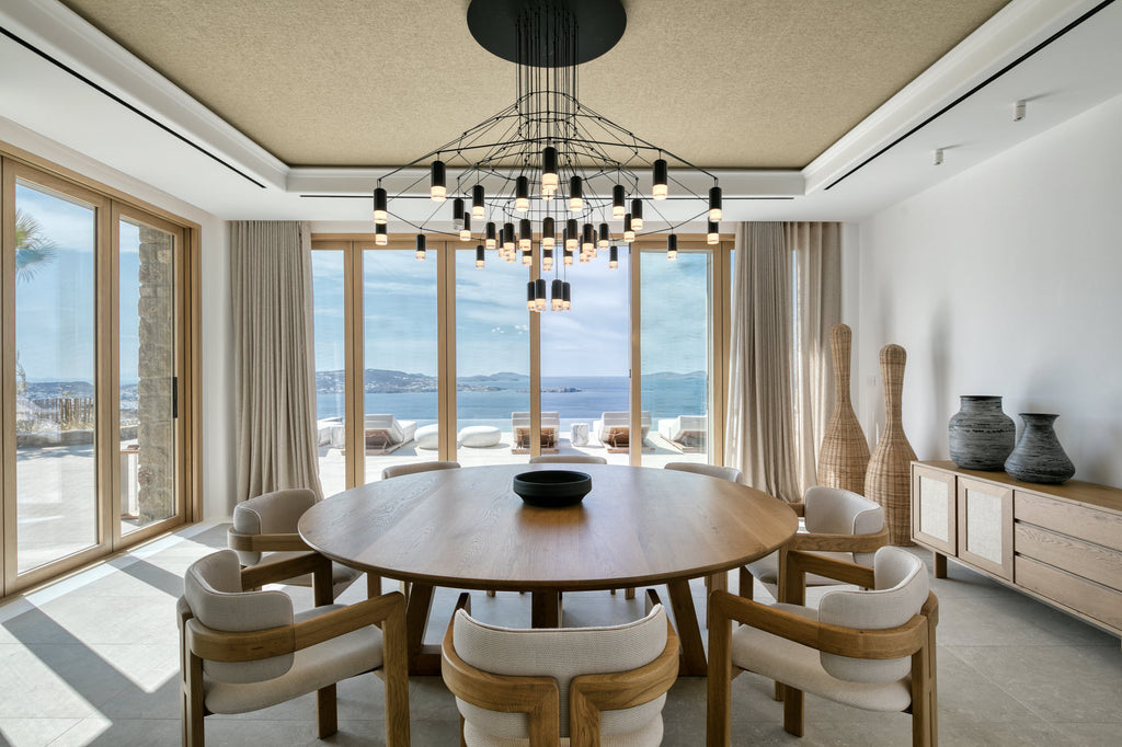 Modern dining room with a round wooden table and chairs, large windows, and a chandelier.