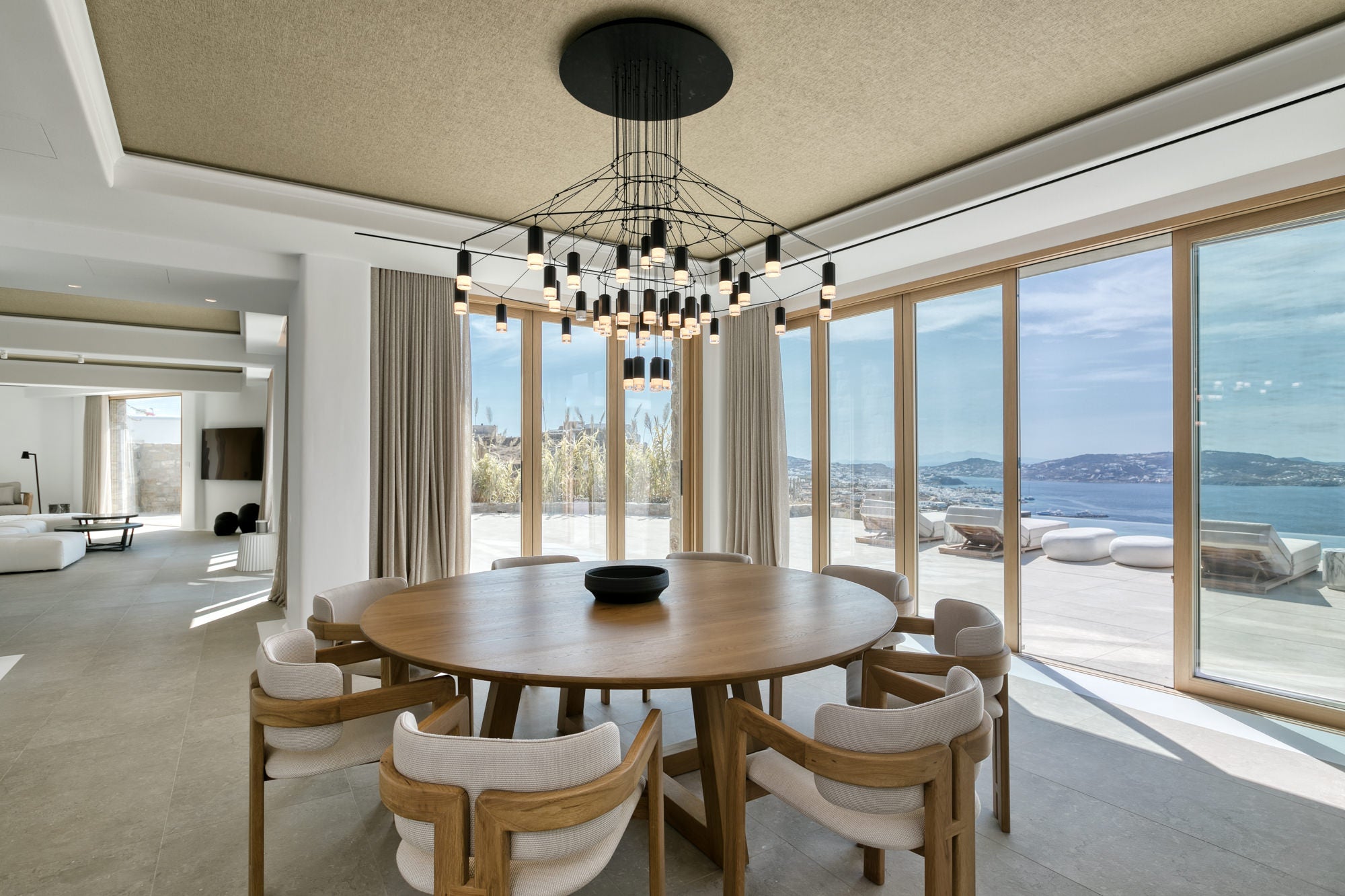Modern dining room with round table and chairs near large windows with a view of the ocean.