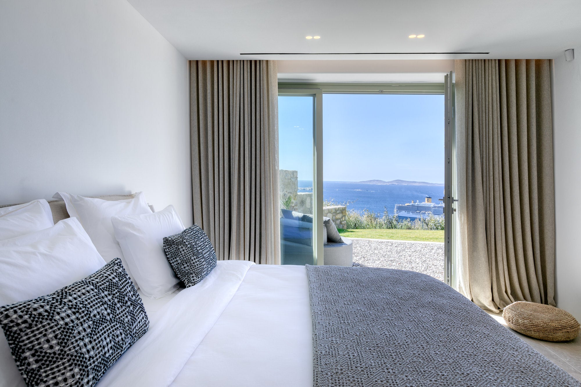 Modern bedroom with a large bed and a view of the ocean through a glass door.