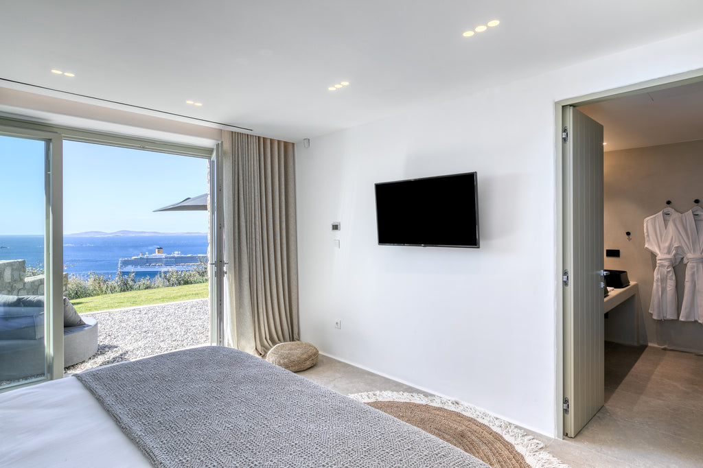 Modern bedroom with ocean view, bed, TV, and open door to bathroom.
