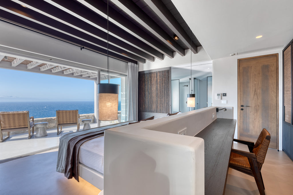 Modern bedroom with ocean view, wooden chairs, and a glass wall.