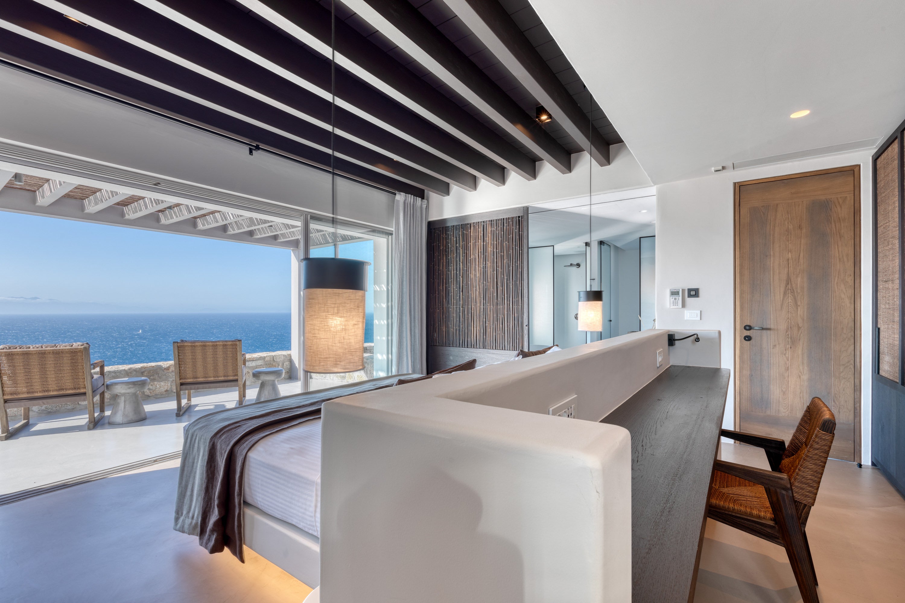 Modern bedroom with ocean view, wooden chairs, and a glass wall.
