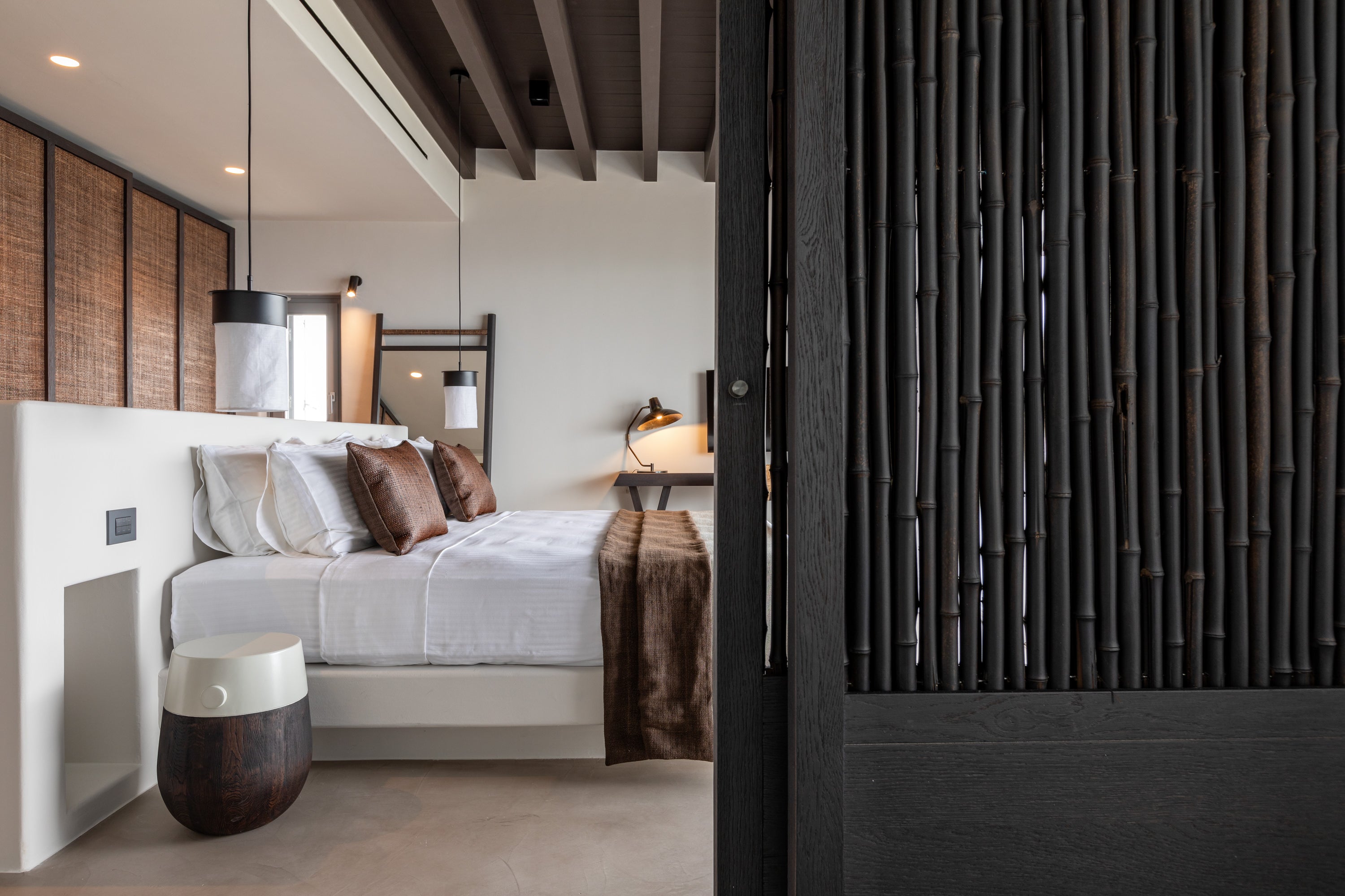 Modern bedroom with a bed, lamp, and decorative pillows, featuring a bamboo wall.