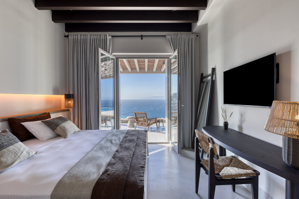 Modern bedroom with ocean view, bed, TV, and chairs.