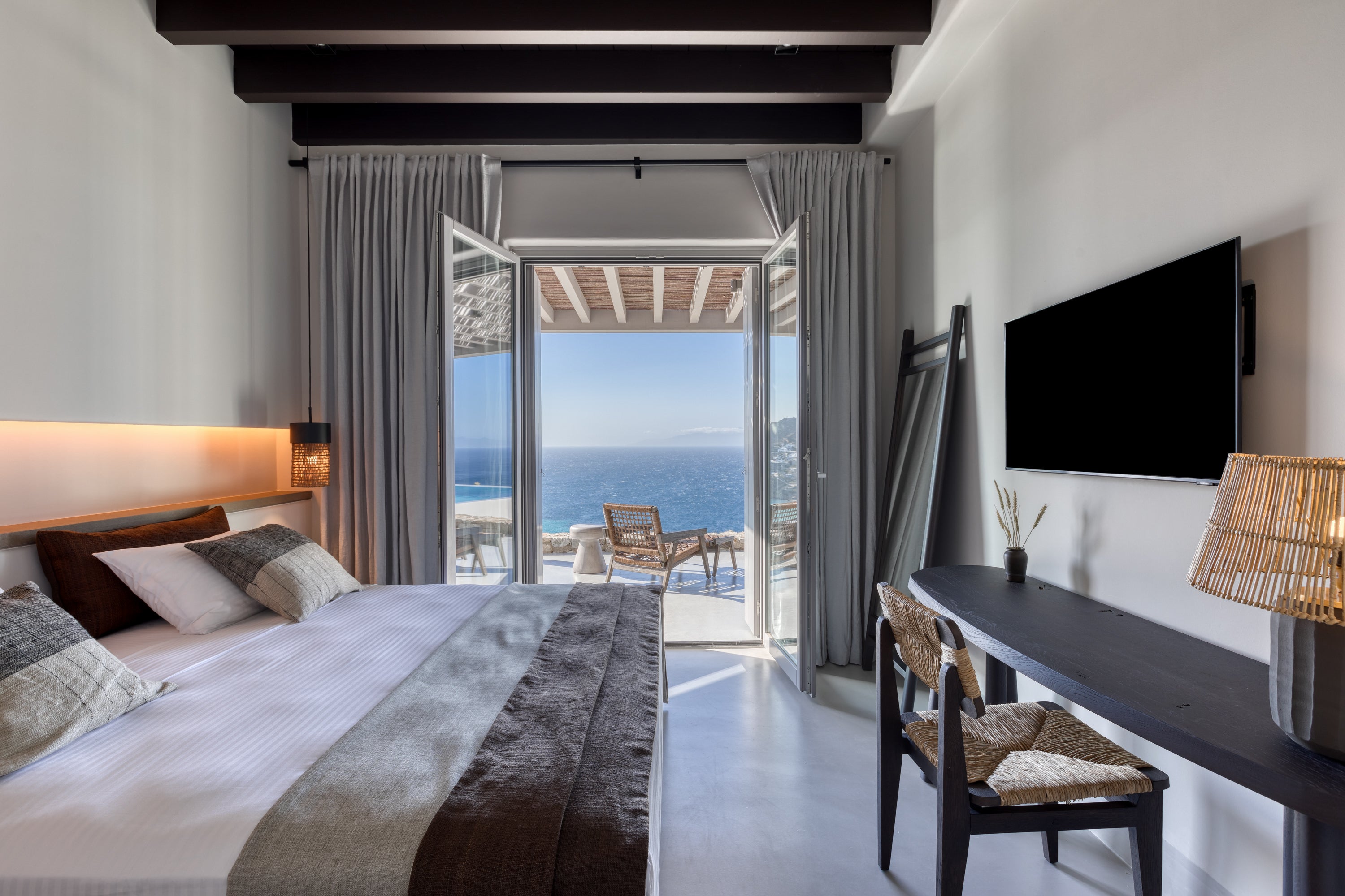 Modern bedroom with ocean view, bed, TV, and chairs.