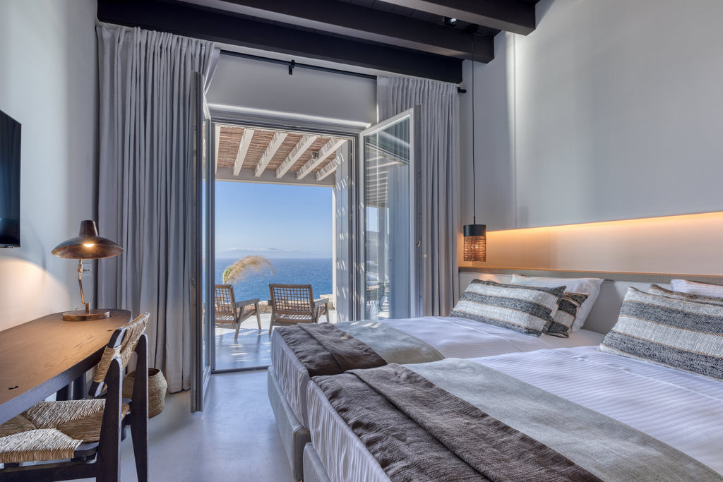 Modern bedroom with a view of the ocean through large glass doors.