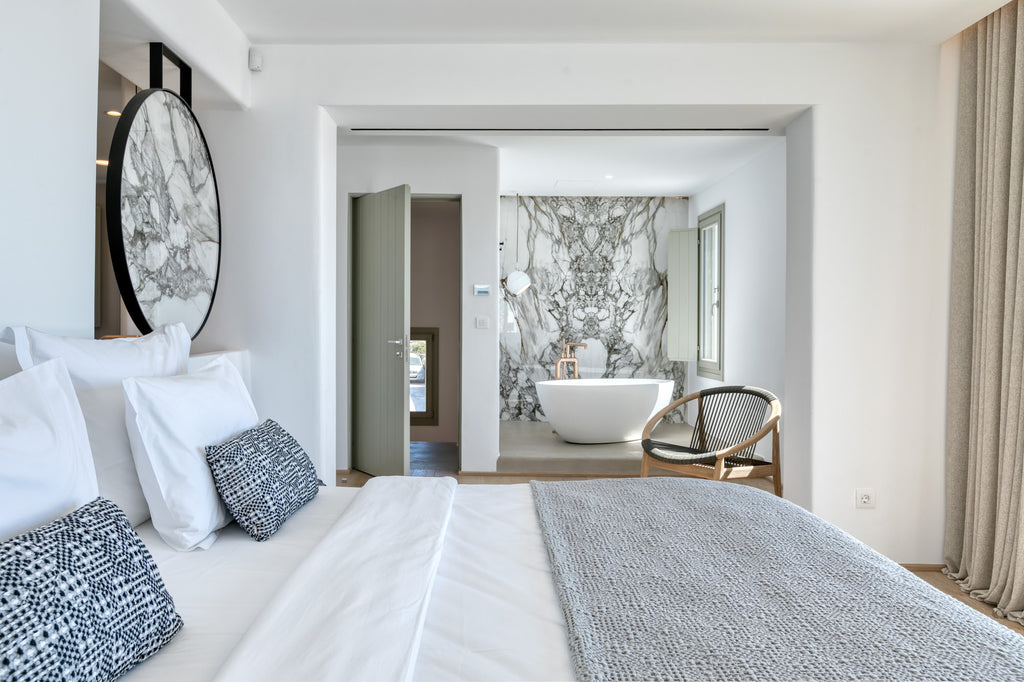 Modern bedroom with a bed, mirror, and bathroom in the background.