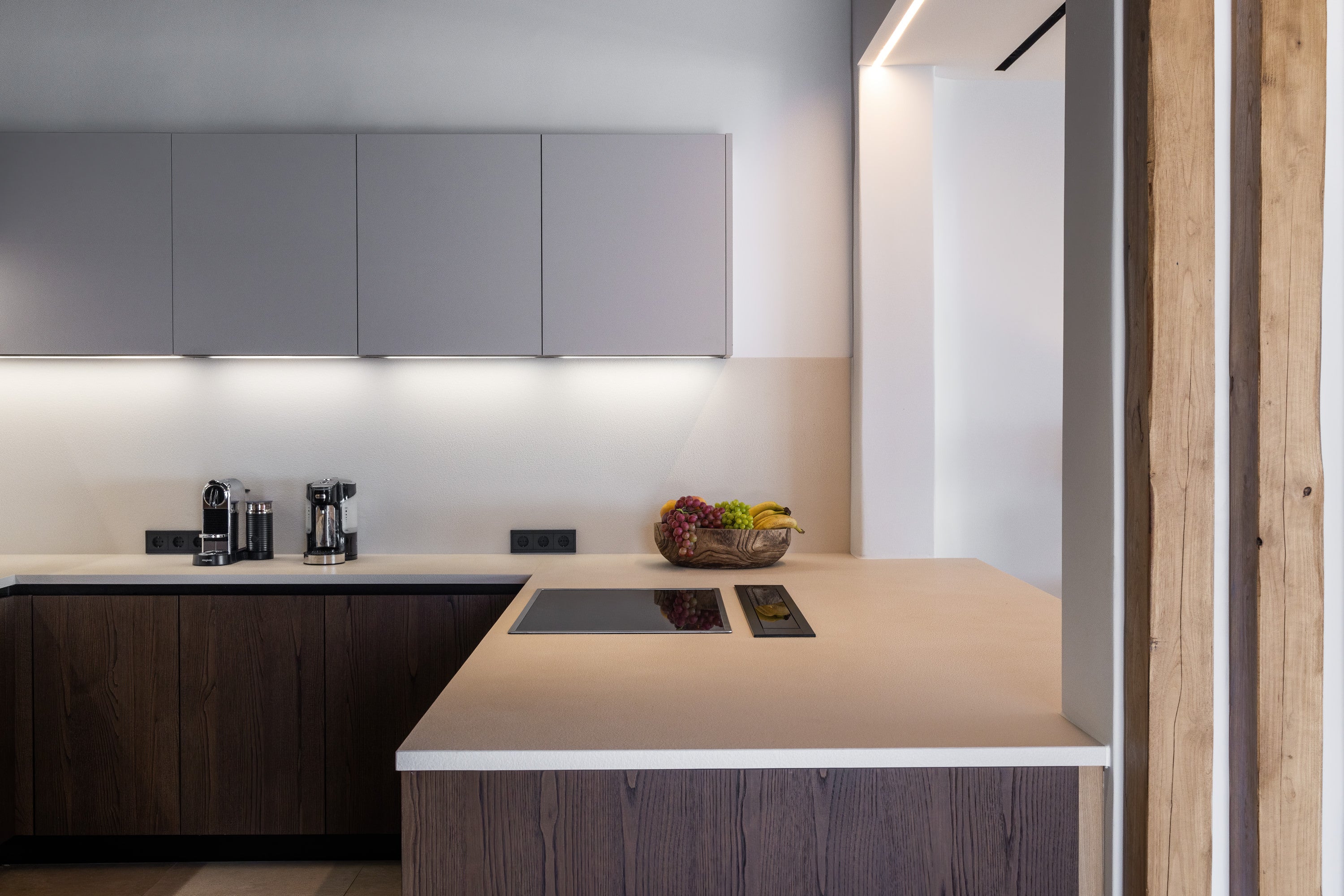 Modern kitchen with gray cabinets, white countertops, and a bowl of fruit on the island.