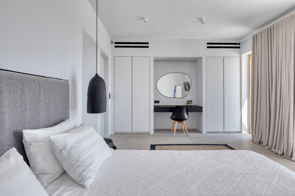 Modern bedroom with gray headboard, white bedding, and a mirror reflecting a desk area.