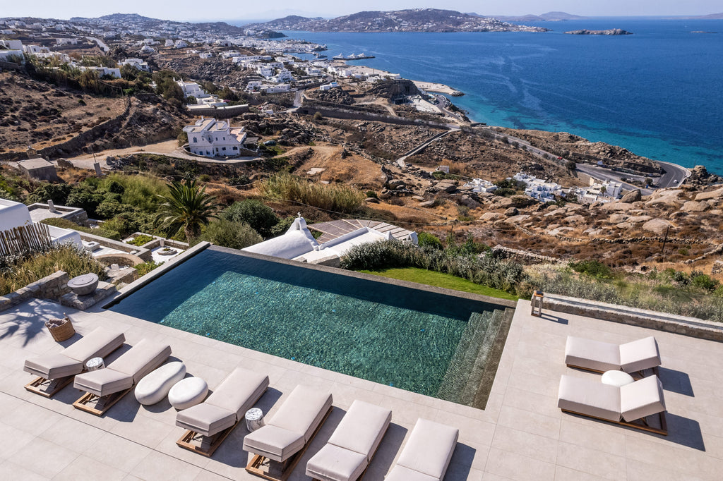 Aerial view of a luxurious villa with an infinity pool overlooking the ocean and coastline.