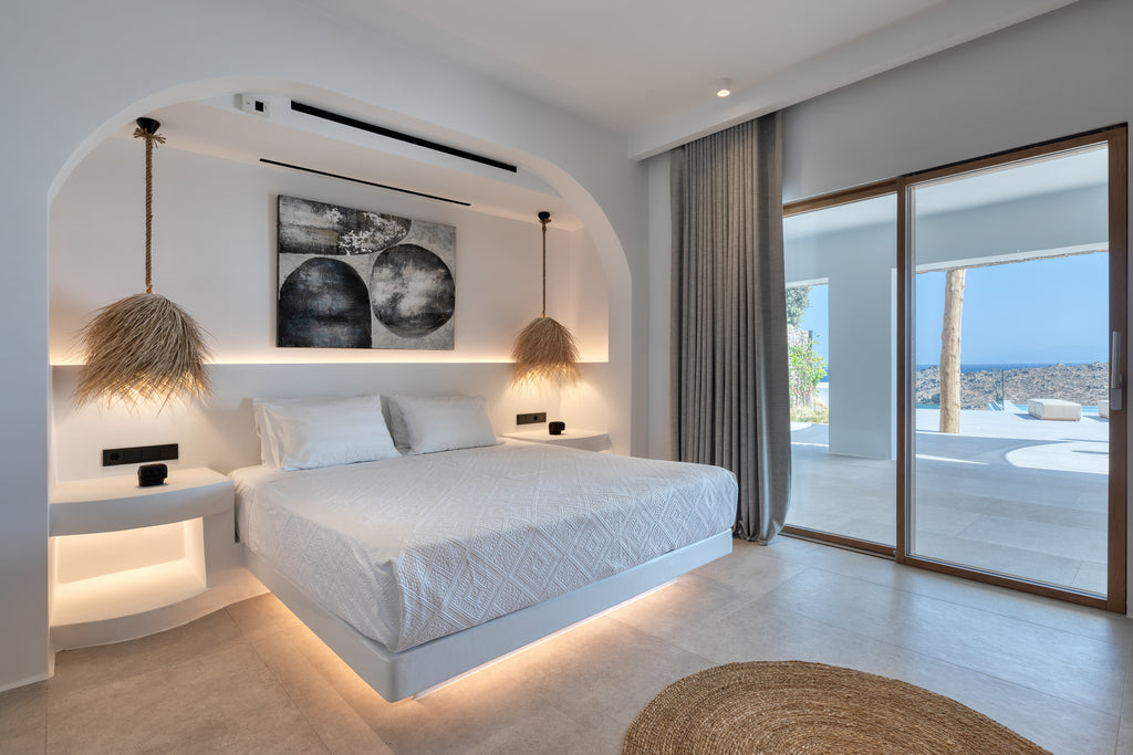 Modern bedroom with a large bed, artwork on the wall, and a view of the ocean through a window.