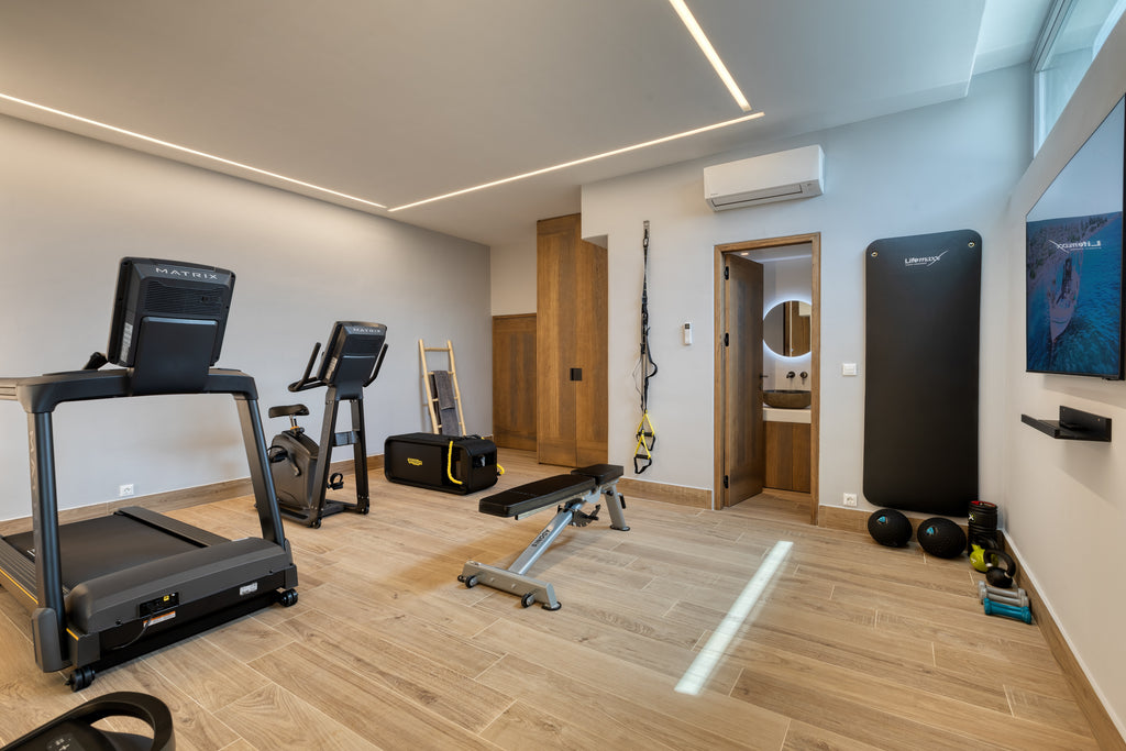 Gym room with treadmill, bench, and various equipment on a wooden floor.