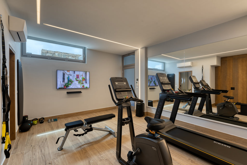 Modern gym with exercise equipment including treadmills and an elliptical machine, featuring a TV on the wall.