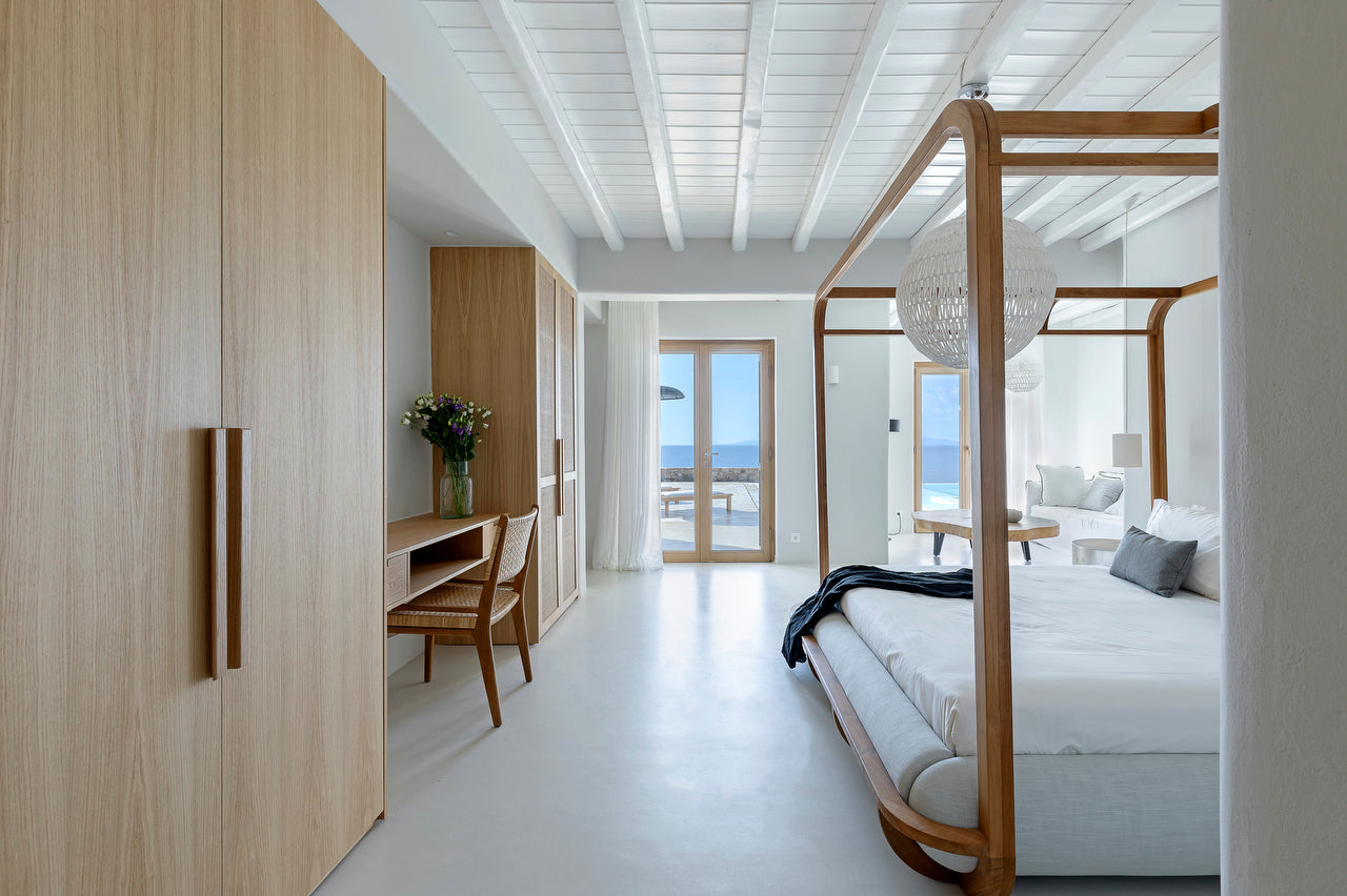Modern bedroom with wooden bed, desk, and large windows overlooking the ocean.
