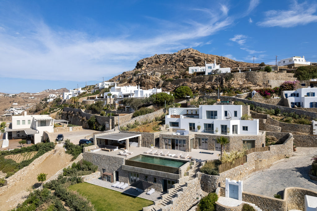 Hillside with white buildings and a pool area under a blue sky.