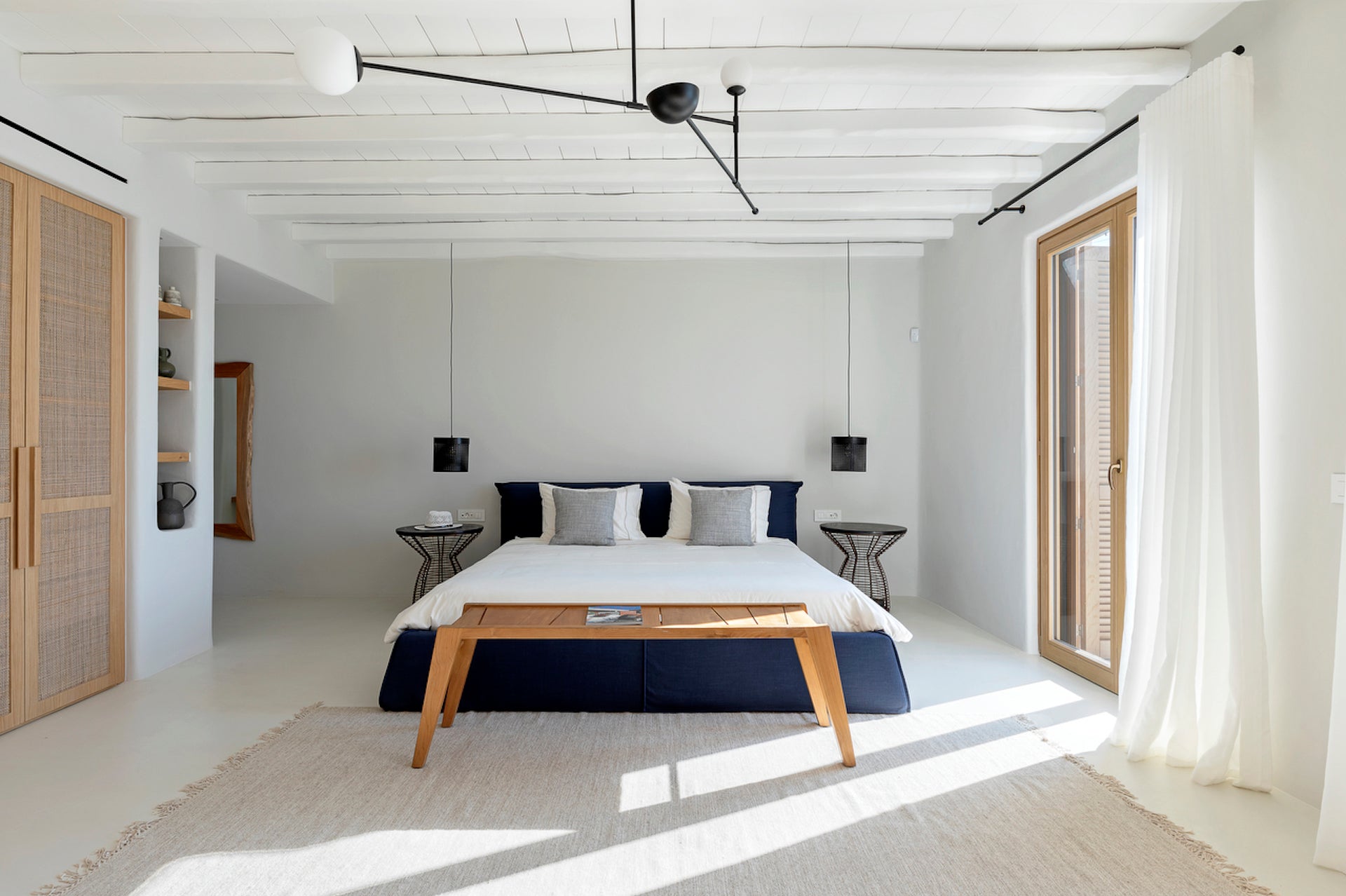 Modern bedroom with a bed, wooden table, and large windows.