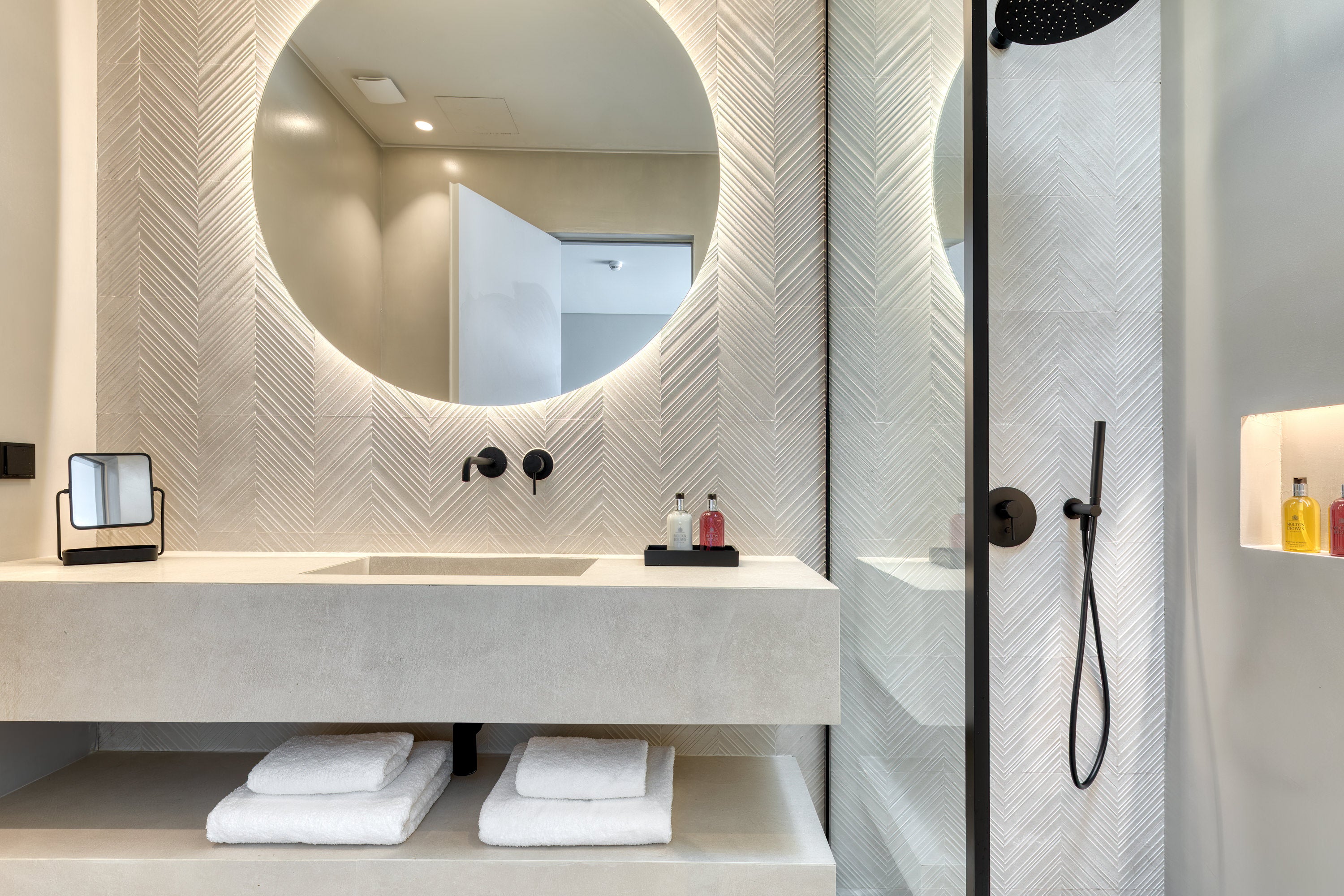 Modern bathroom with round mirror, sink, and shower area.