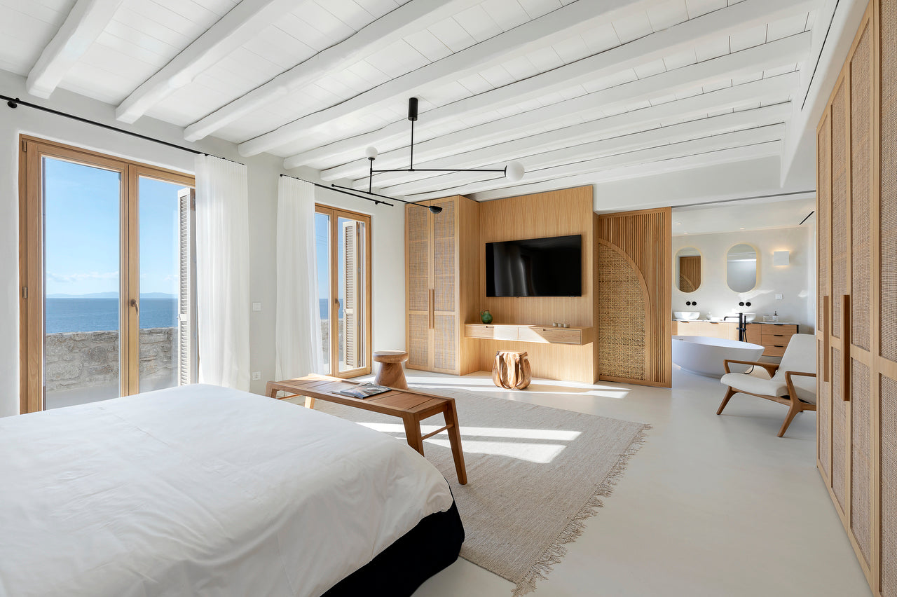 Modern bedroom with wooden furniture, TV, and large windows overlooking the ocean.