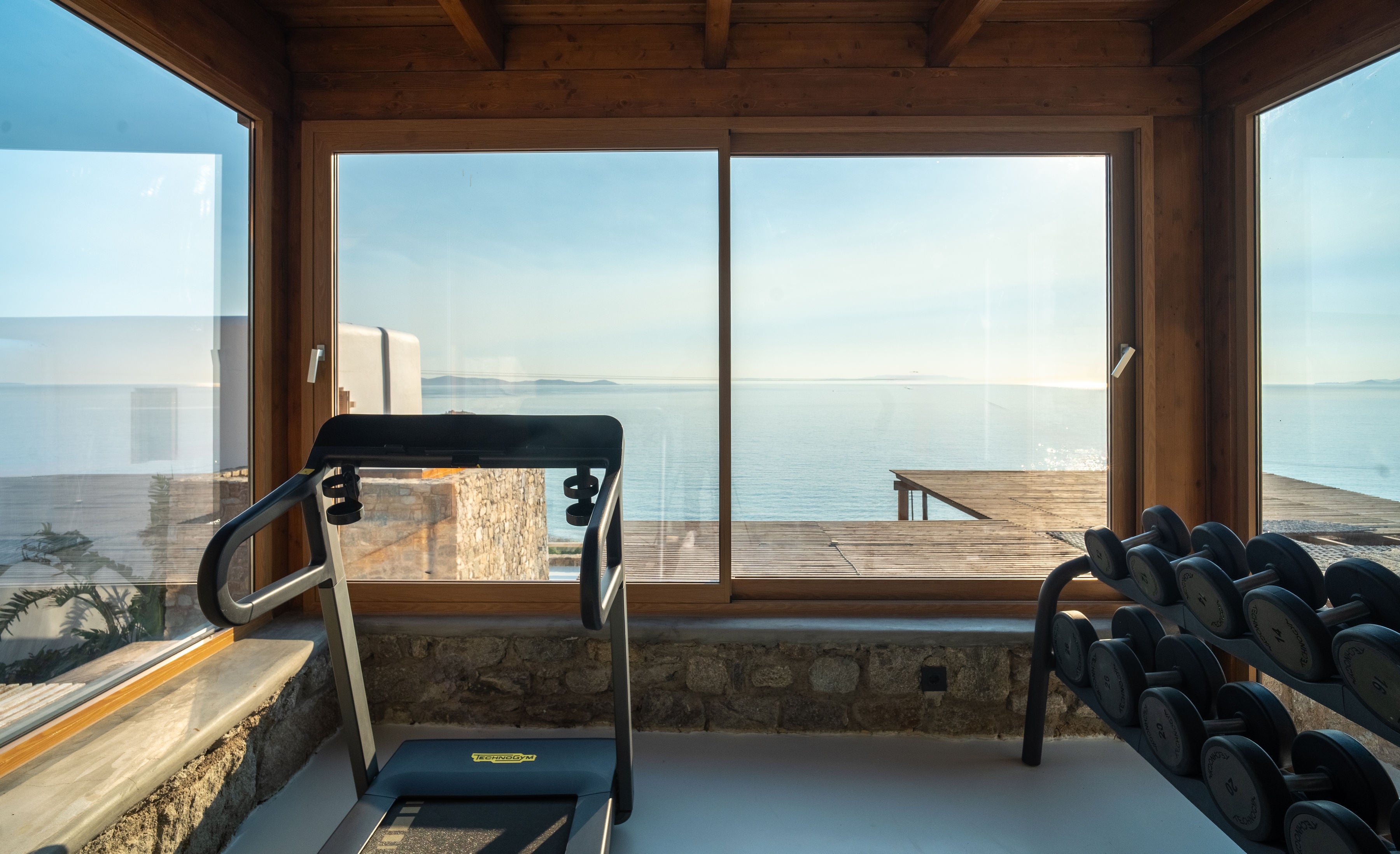 Gym equipment with a scenic view of water and sky through large windows.