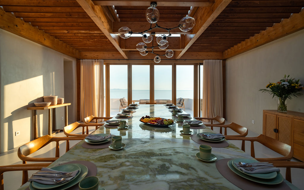 Dining room with a long table set for a meal, large windows, and wooden ceiling.