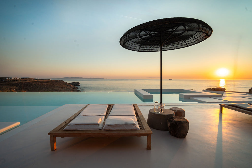 Sunset by a poolside with lounge chairs and an umbrella.