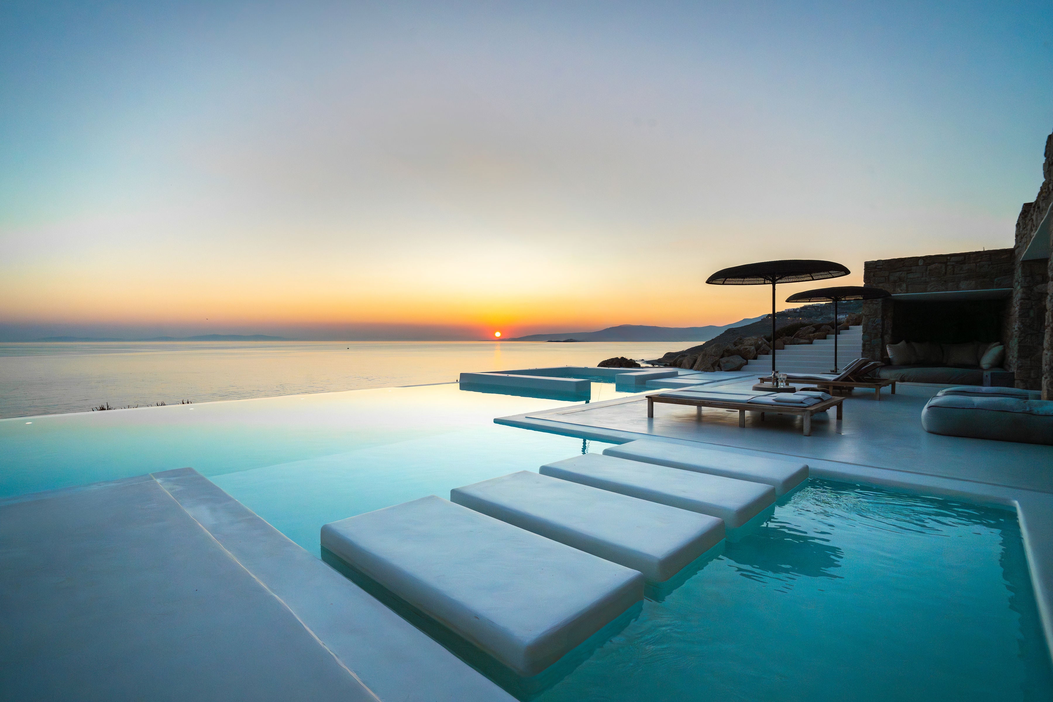 Pool area with lounge chairs and an umbrella at sunset with a scenic view of the ocean.
