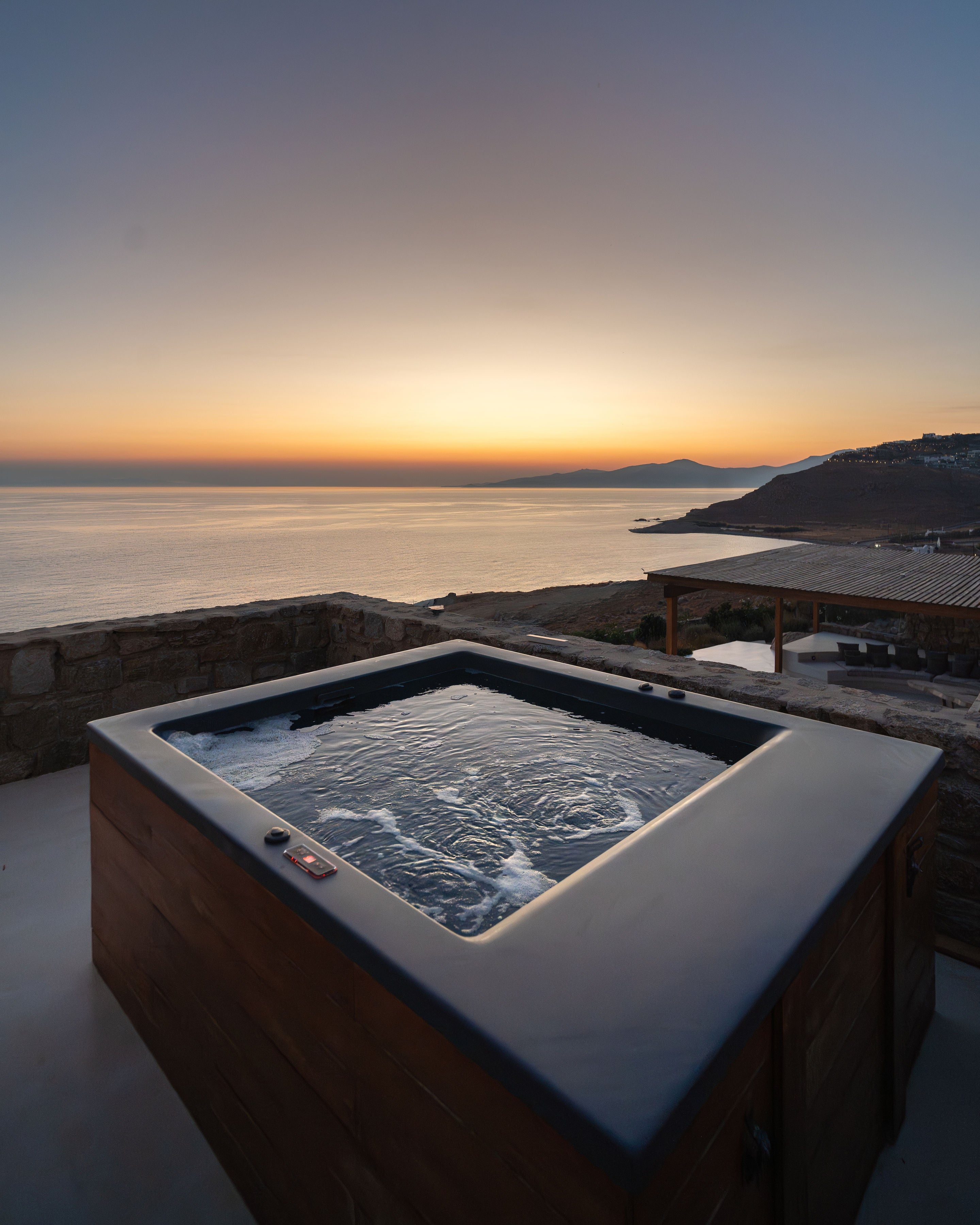 Hot tub with a scenic view of a sunset over water and mountains.